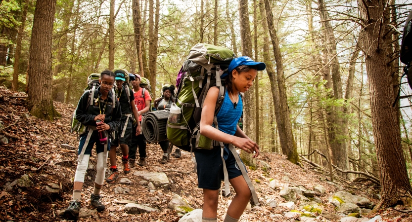 A group of young people wearing backpacks high through a wooded area 